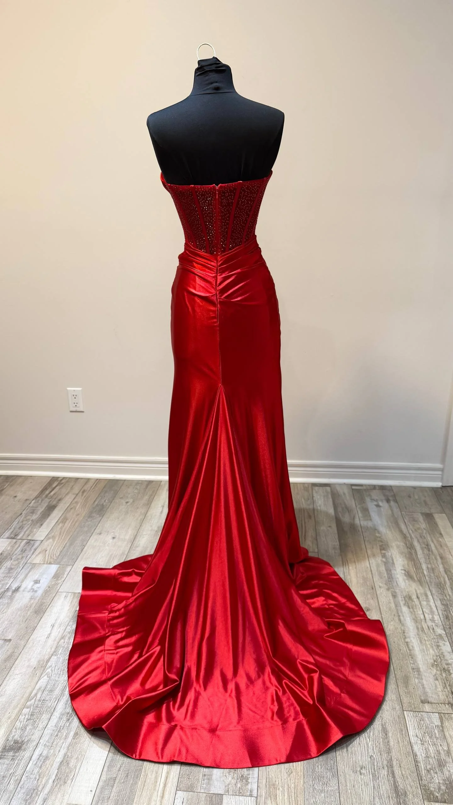 A black mannequin dressed in a stunning red satin evening gown with a fitted, jewel-embellished bodice, high neckline, and flowing train.