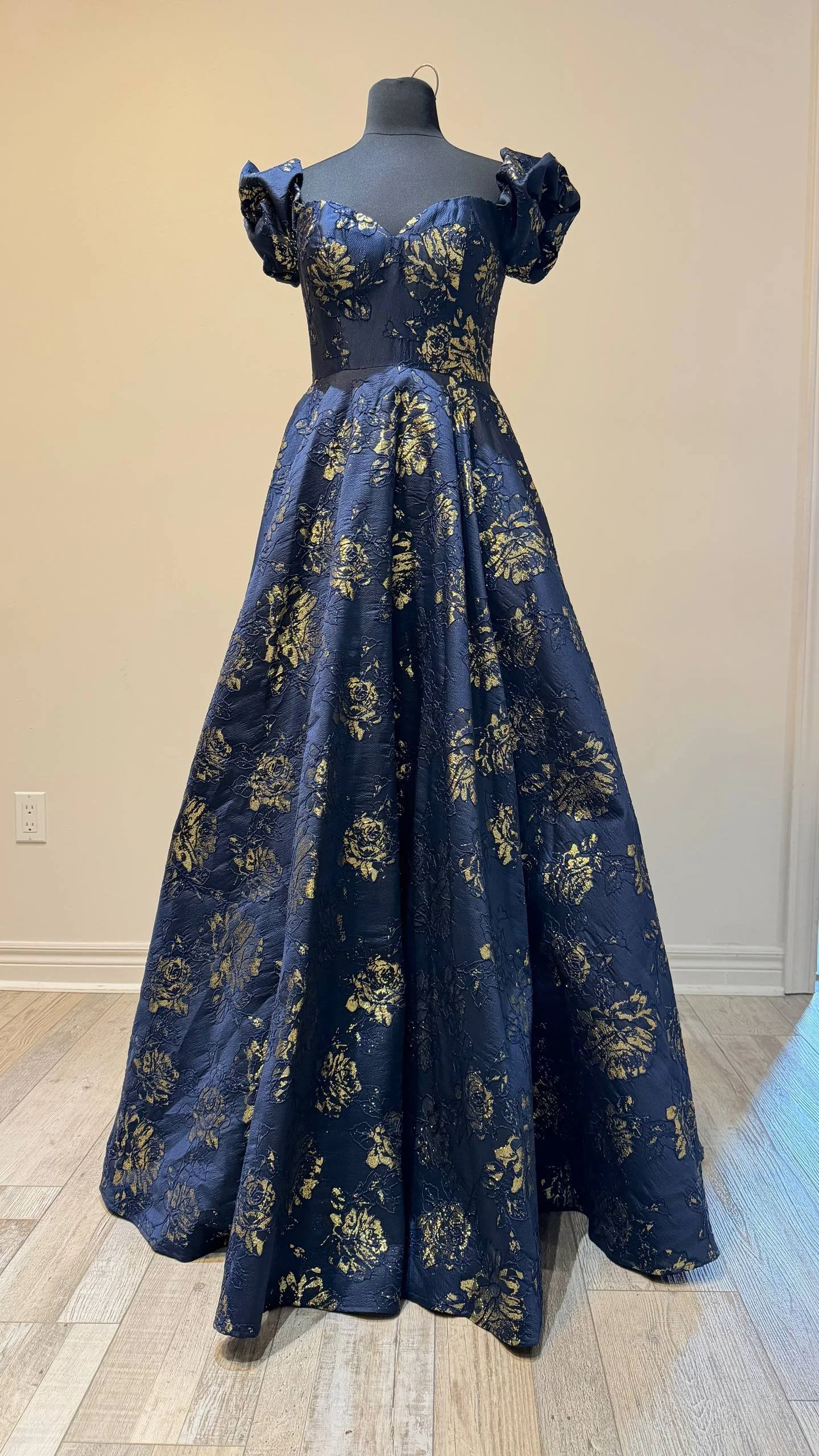 A dark blue and gold floral patterned ball gown with puffed short sleeves displayed on a dress form.