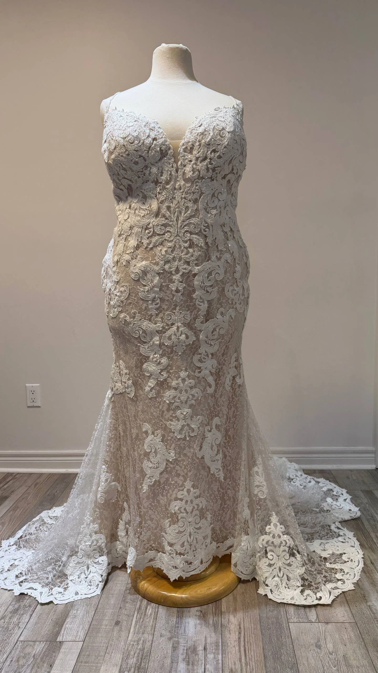 A wedding dress displayed on a mannequin, featuring intricate lace and floral embroidery, with a fitted bodice and a flowing train.