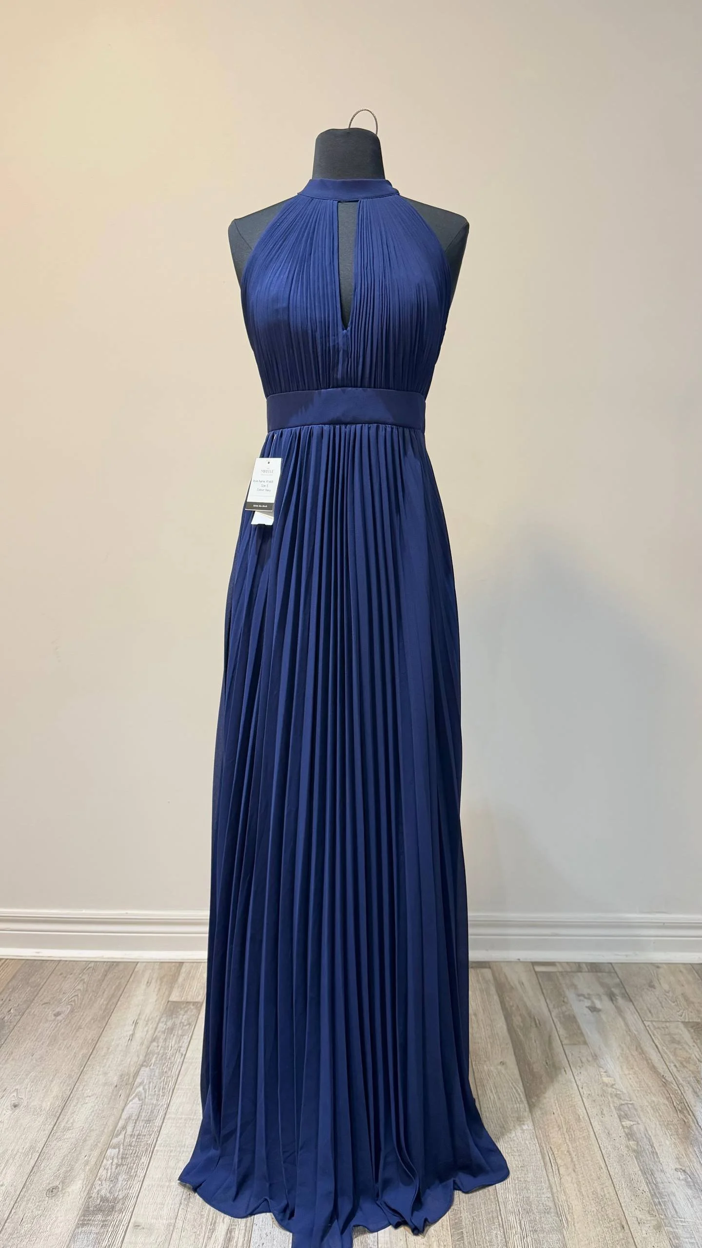 A long, pleated royal blue evening gown displayed on a mannequin with a halter neckline and a keyhole cutout.
