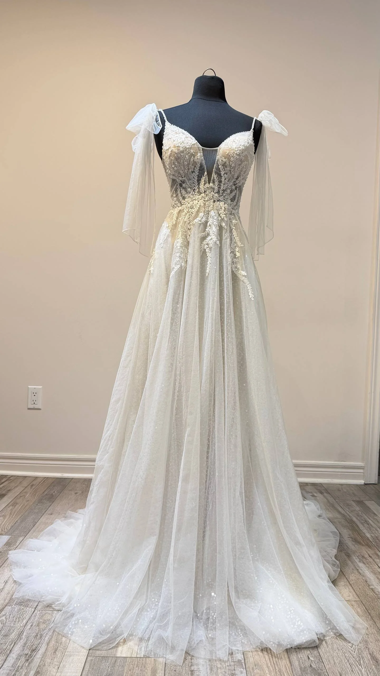 An elegant wedding gown with lace and embroidered details displayed on a black mannequin.
