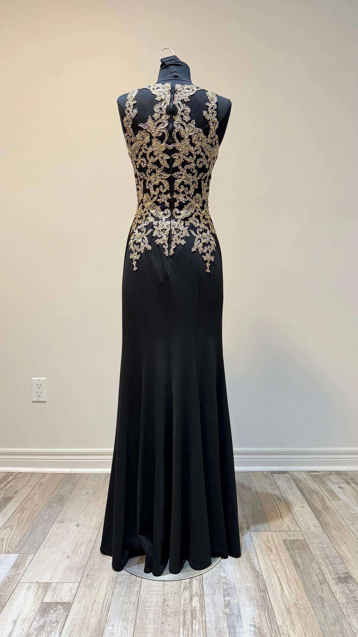 A black evening gown with gold embroidery displayed on a mannequin.
