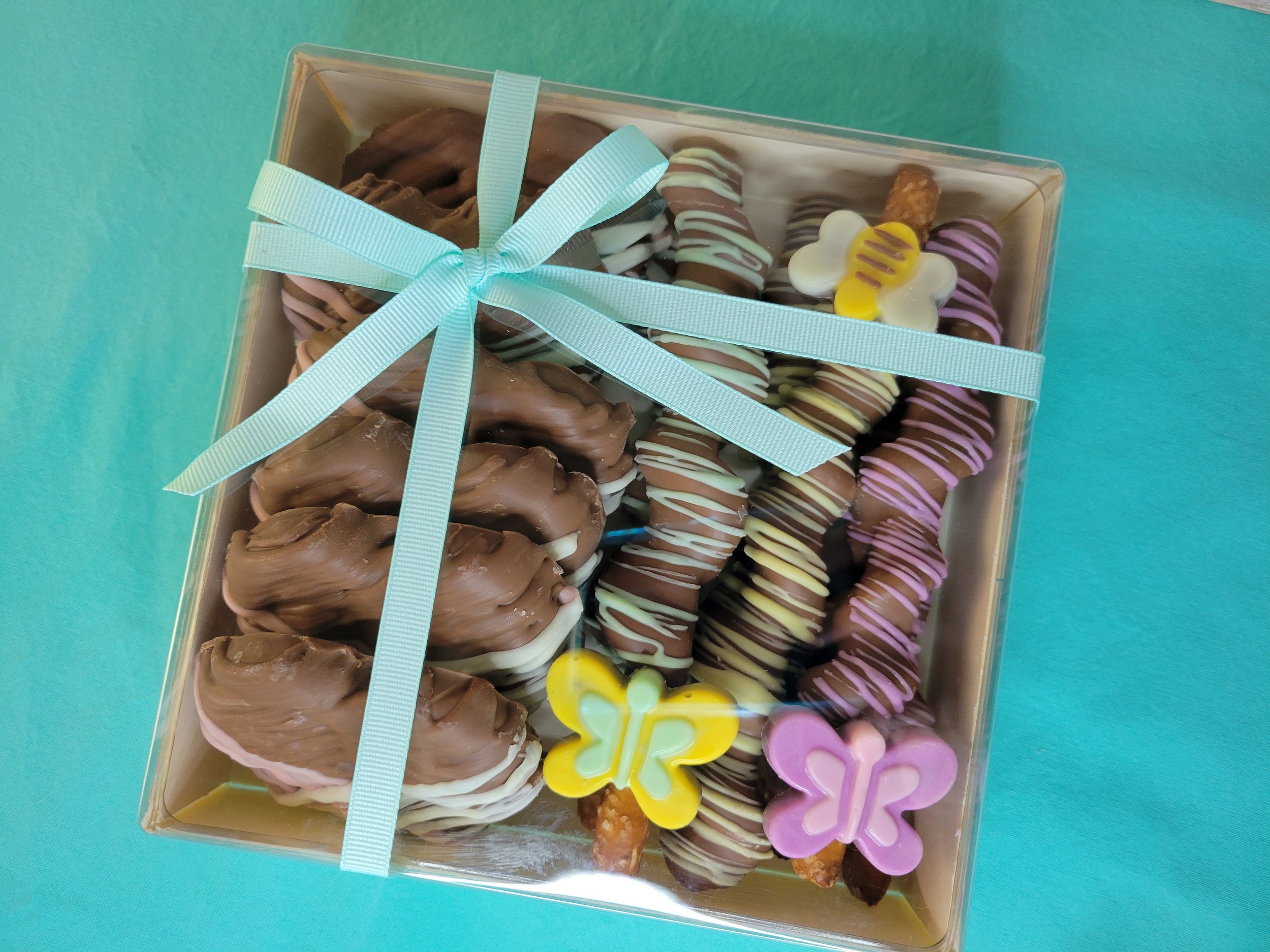 A gourmet goodie box filled with assorted chocolate-covered pretzels decorated with colorful drizzles and butterflies in a gift box with an aqua ribbon