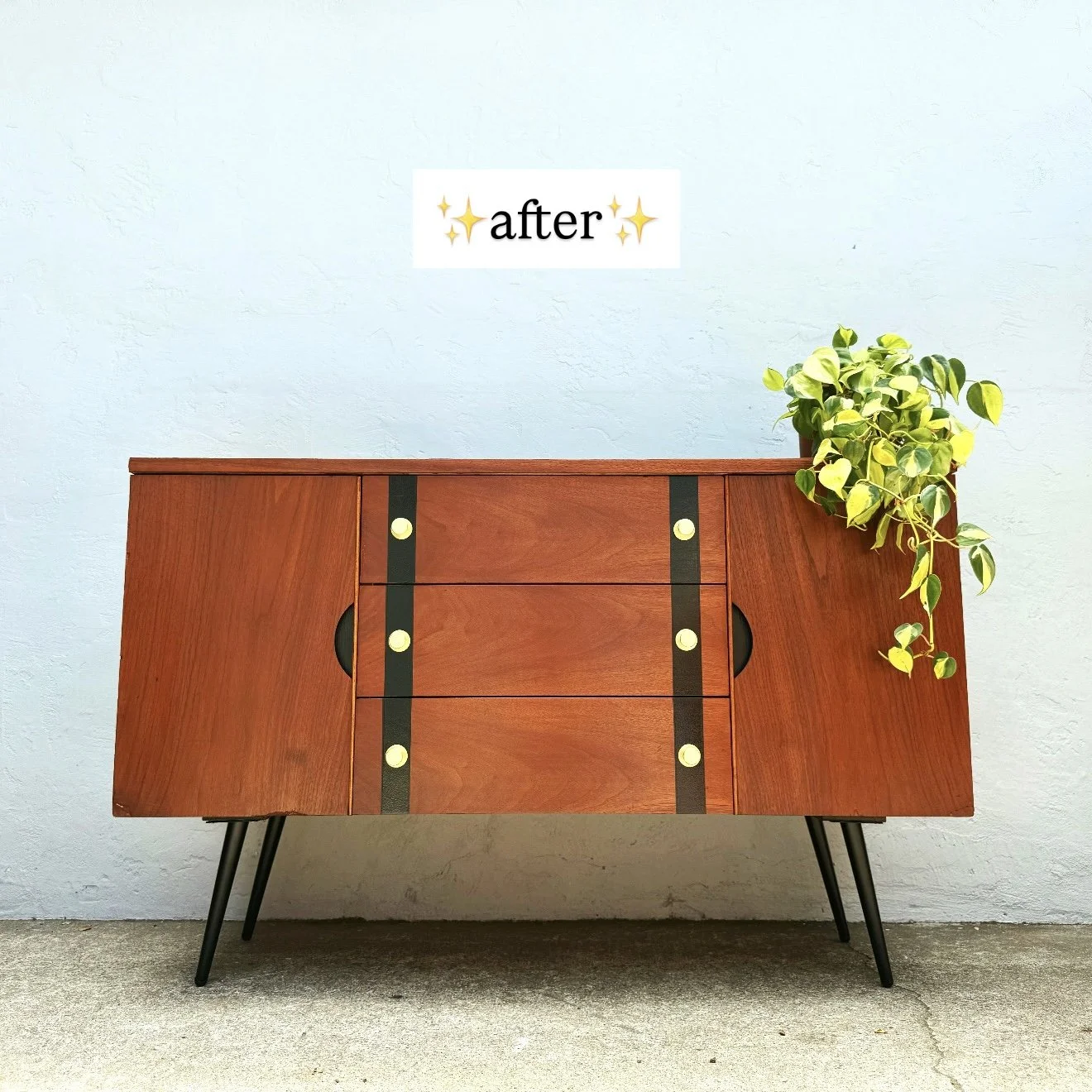 Mid-century modern wooden sideboard with black accents and four drawers, sitting against a light blue wall with a potted green plant on the right side, and a white sign that says "after" with star emojis above.