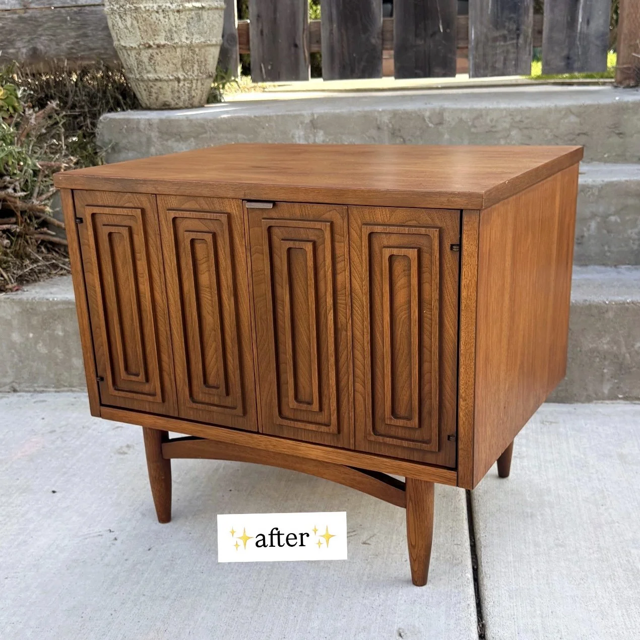 A wooden cabinet with four doors, featuring geometric carved patterns, standing outdoors on a concrete surface near some stairs and bushes, with a "✨after✨" label at the bottom.