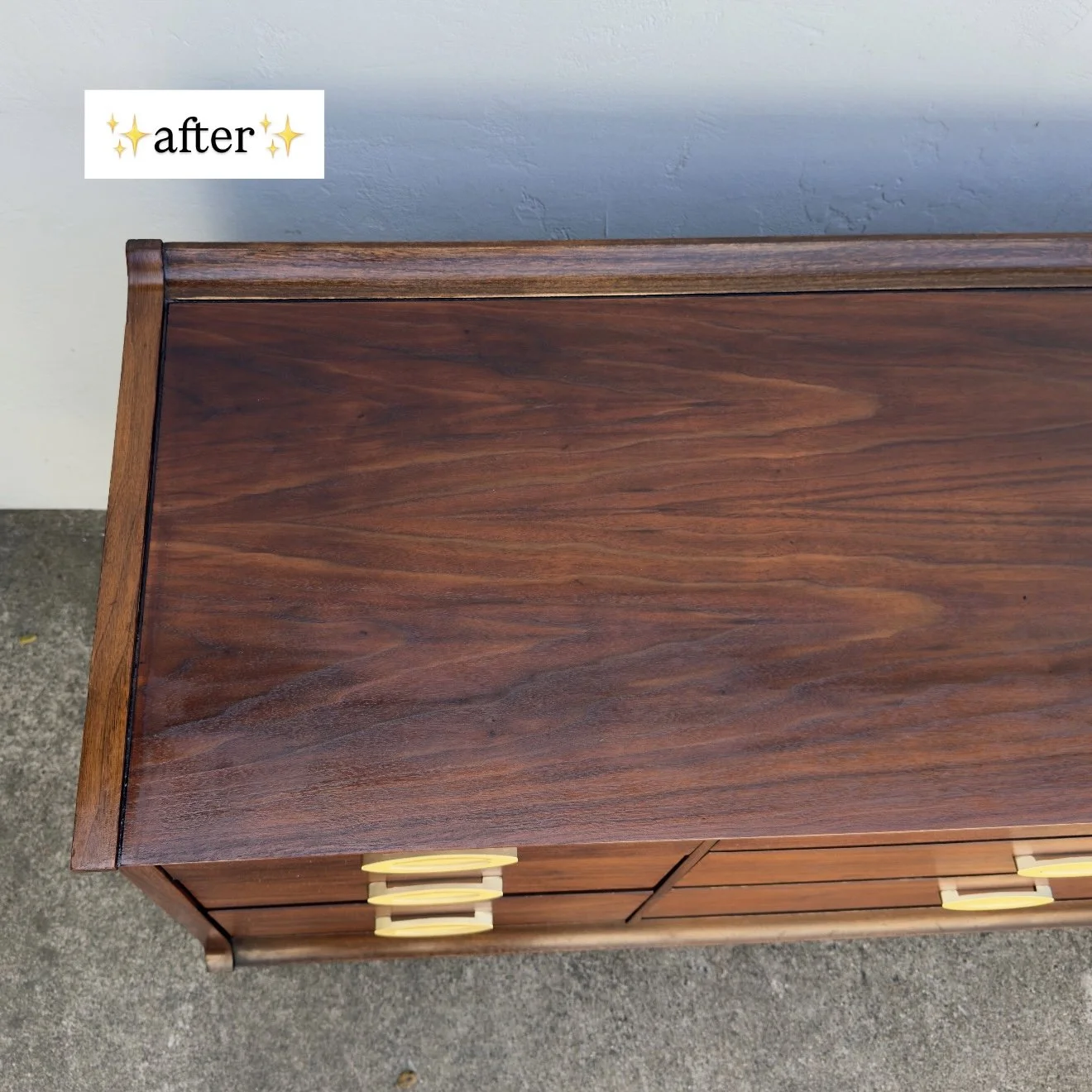 Top view of a vintage wooden dresser with a flat surface and yellow handles, placed against a light blue wall.
