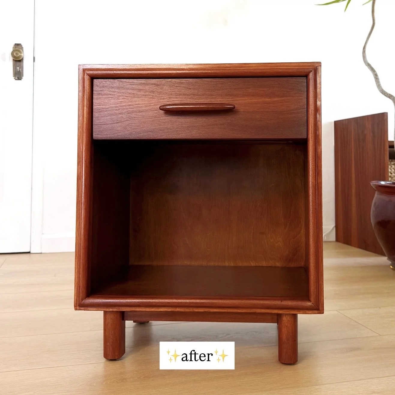 A vintage wooden nightstand with a small drawer at the top, finished in a warm wood tone, standing on four short legs, with the word 'after' and sparkles at the bottom.