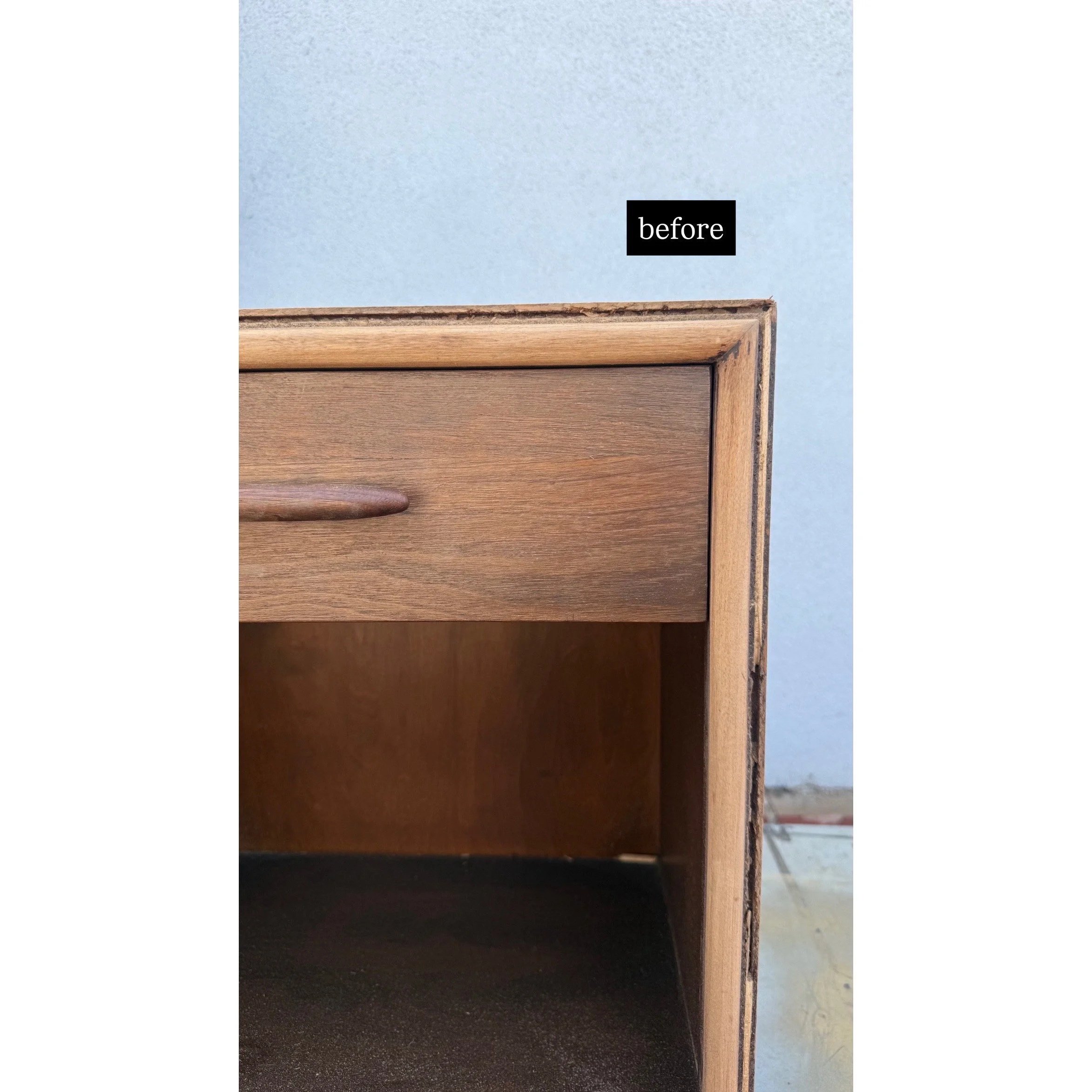Close-up of a wooden desk with a drawer, showing the corner with a small black label that says 'before' against a blue wall background.