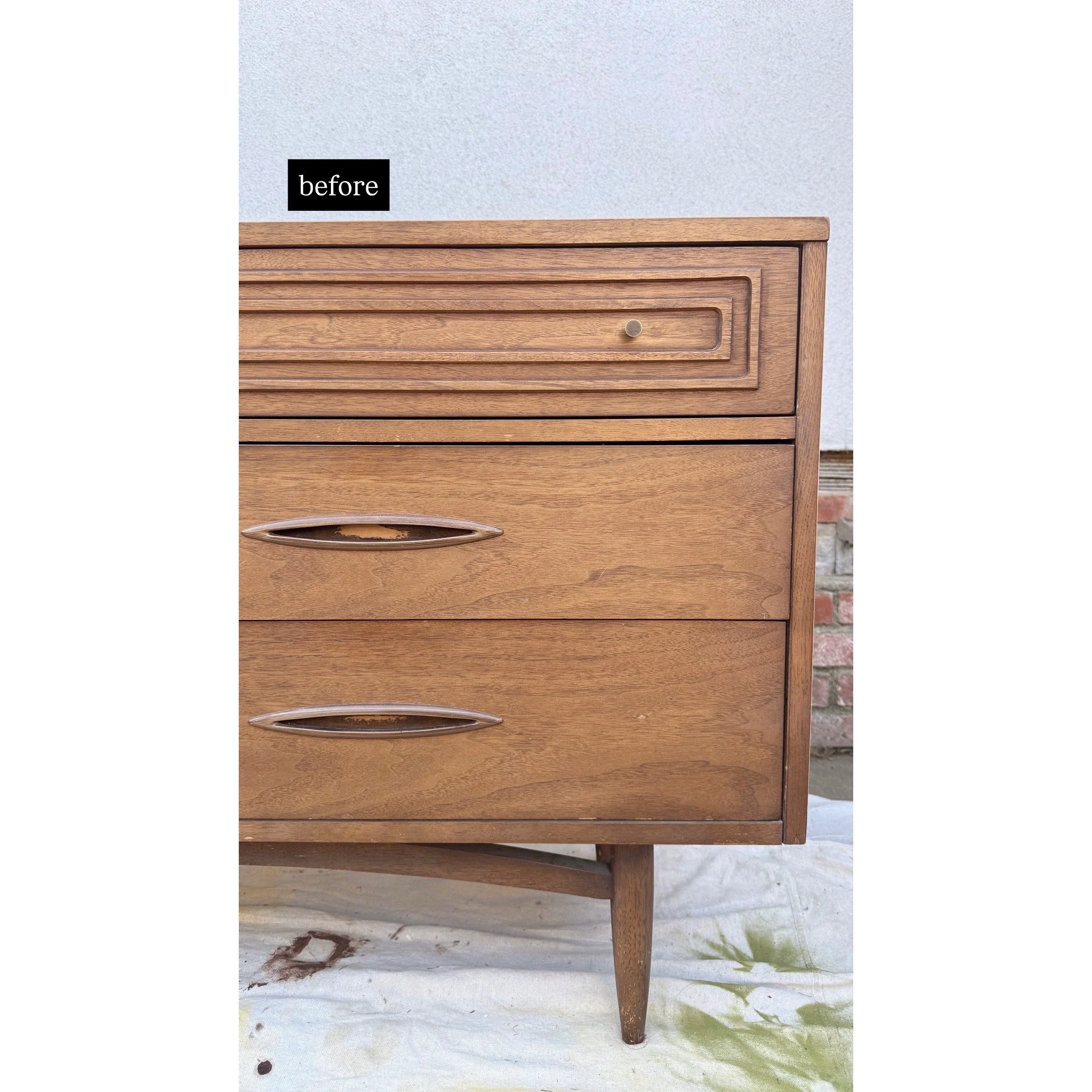Wooden dresser with two drawers, one smaller top drawer and two larger bottom drawers, placed outdoors on a sheet with a brick wall in the background.