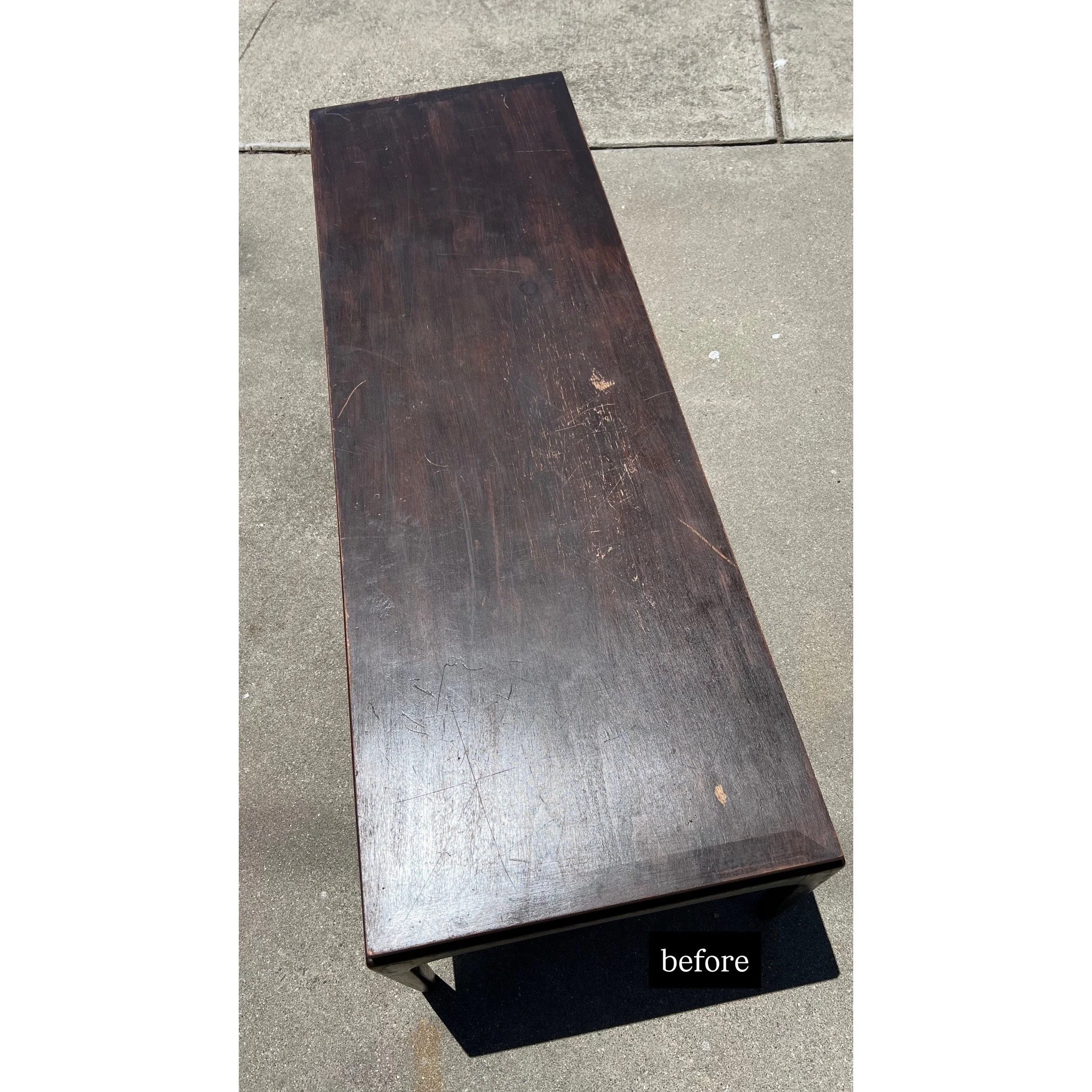 A long, dark wooden bench with visible scratches and marks, situated on a concrete sidewalk. The word 'before' is labeled at the bottom of the image.