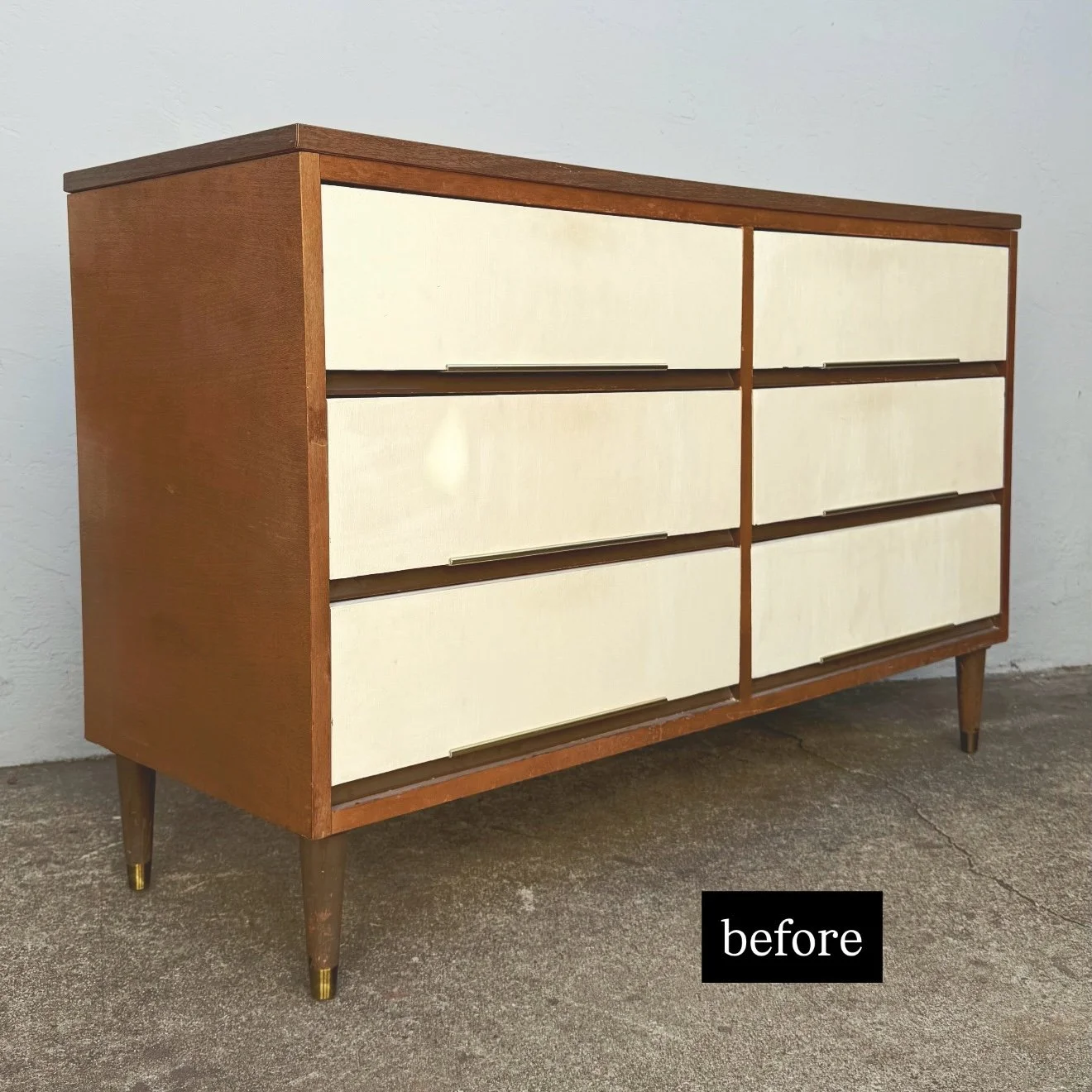 Vintage wooden dresser with cream drawers on a concrete floor against a white wall.