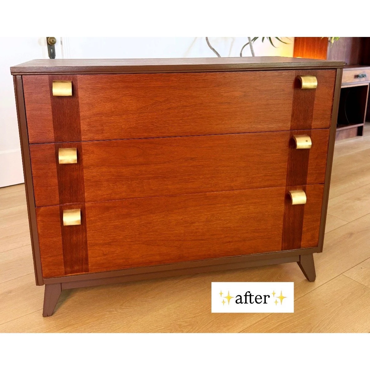 Wooden dresser with mid-century modern design featuring three drawers and gold-colored handles, placed on a wooden floor.