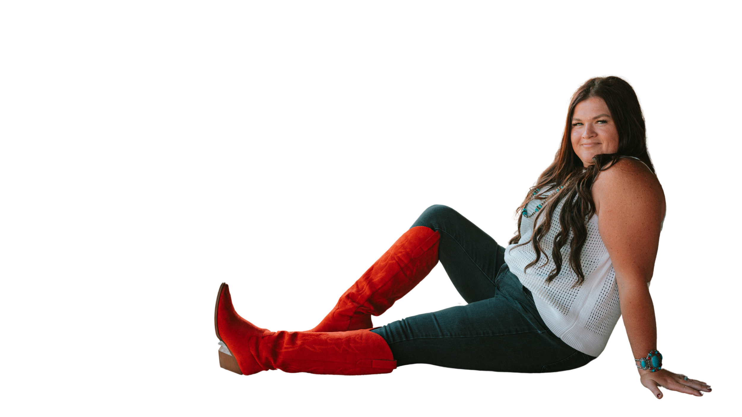 Ryann with long brown hair, wearing a sleeveless white top, dark jeans, and red boots, sitting on the ground and leaning back on her hands. She is smiling slightly and looking at the camera, with a colorful background.