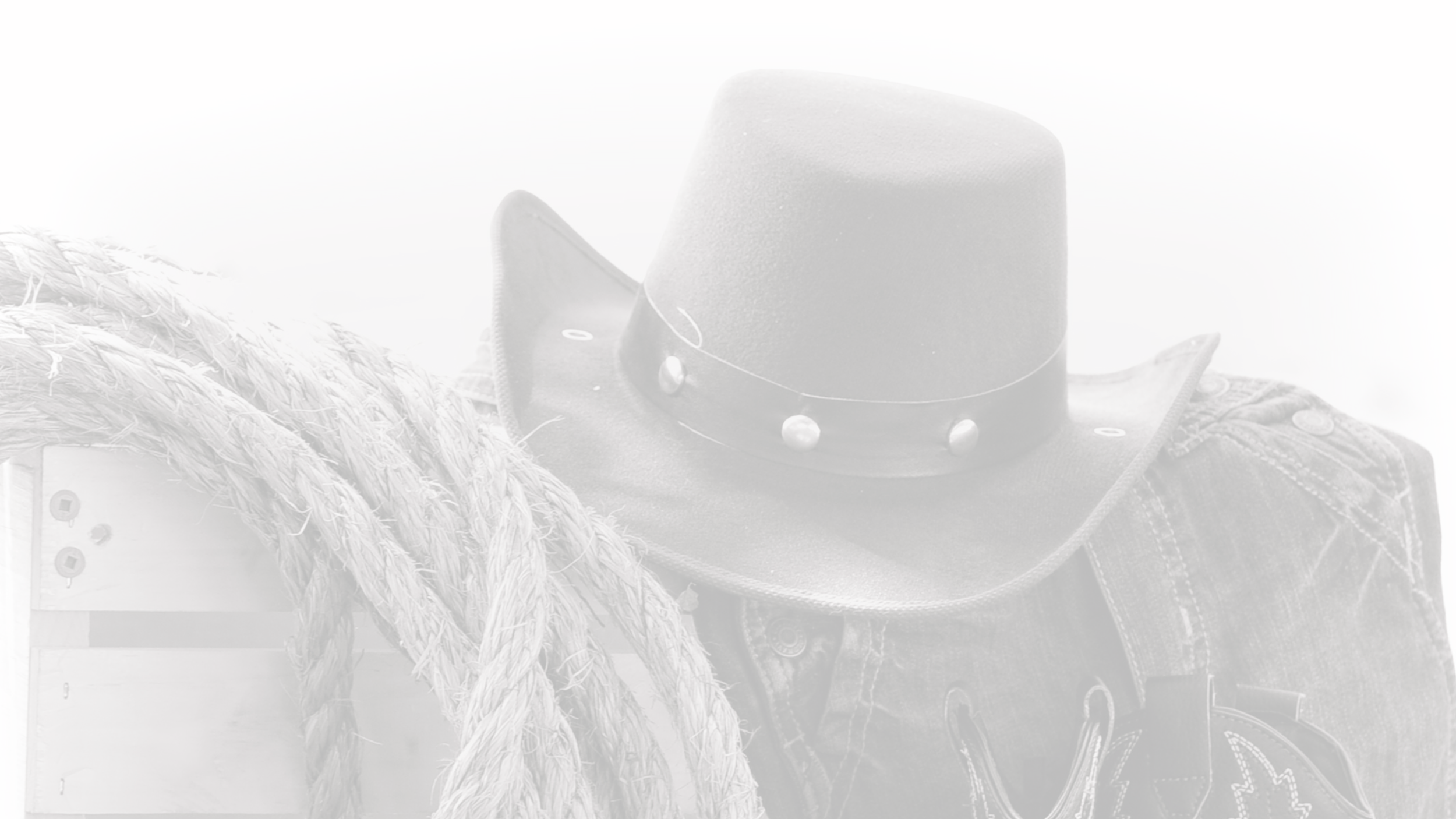 A cowboy hat with a wide brim and decorative studs, placed on a pair of denim jeans. Next to the hat are thick, twisted ropes and a wooden box or crate.