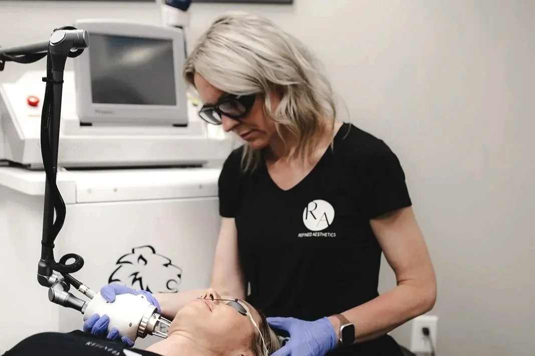 A woman receiving a cosmetic procedure on her face with a handheld device, while a professional wearing gloves assists.