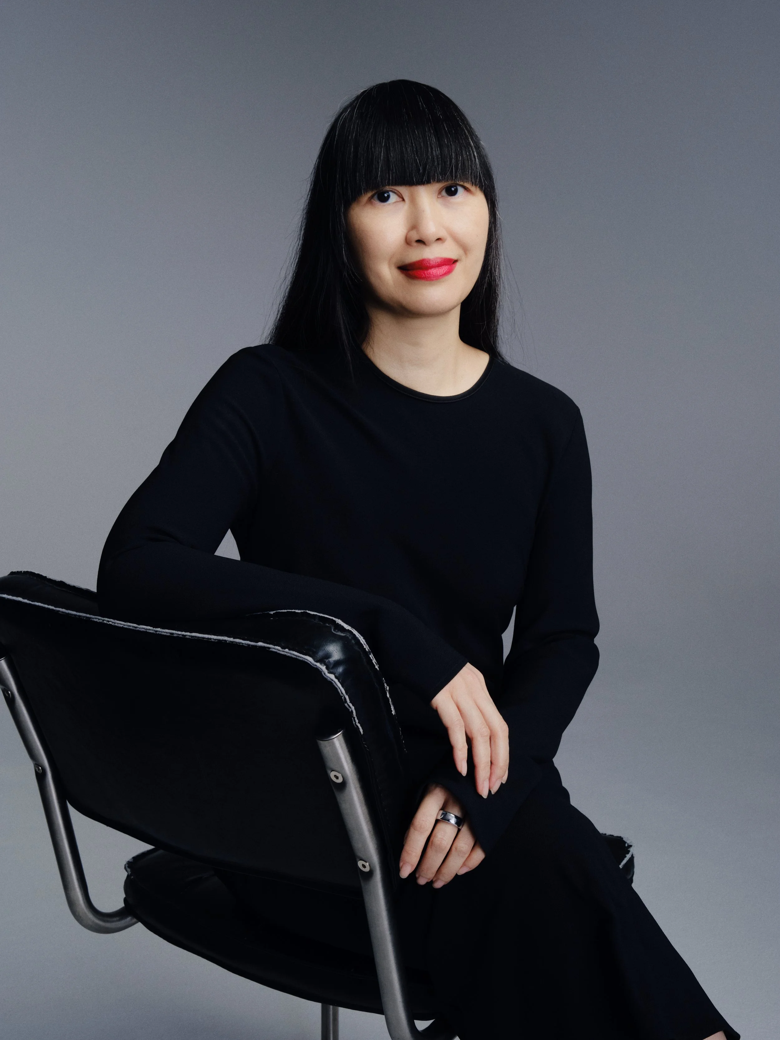 Portrait of Deanna Chow seated on a chair wearing a black dress and looking at the camera with a soft smile