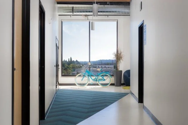 Large, brightly lit hallway in a modern Portland, Oregon office featuring expansive floor-to-ceiling windows and a classic blue Schwinn bicycle for employees to ride throughout the workspace
