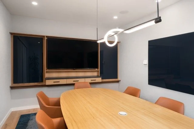 Modern commercial office conference room in Hillsboro, Oregon featuring a white oak conference table, custom white oak casework, modern pendant lighting, and integrated TV display for presentations