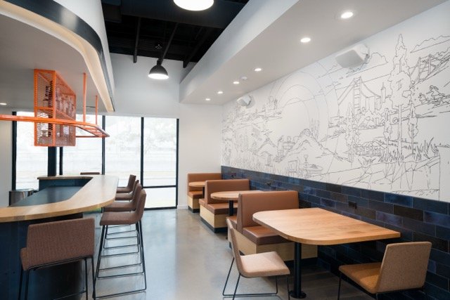 Employee kitchen lounge in a creative office featuring warm leather banquette seating, custom mural artwork, bar-height seating, and oversized industrial pendant lights in Portland, Oregon