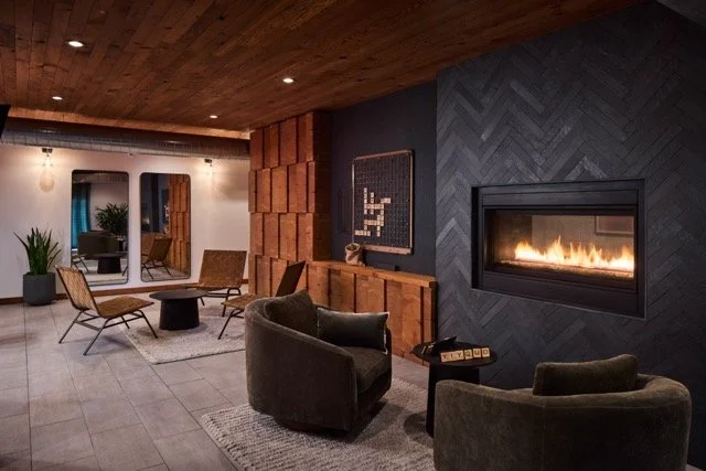 Modern residential lounge in a multifamily property in Portland, Oregon featuring wood-clad walls, a gas fireplace, and a wall-mounted Scrabble game for community engagement