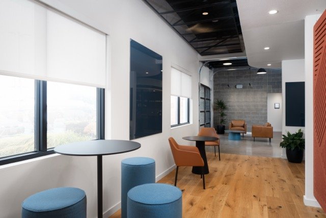 Modern commercial office interior featuring white oak floors, blue counter stools, Lutron roller window shades, and modern architectural lighting in Hillsboro, Oregon