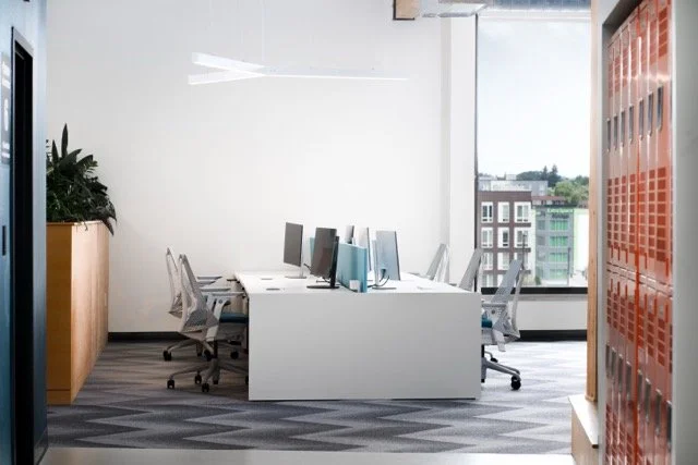 Creative office in Portland, Oregon with expansive floor-to-ceiling windows showcasing city views, orange employee lockers, and a large white desk system for collaborative workspaces