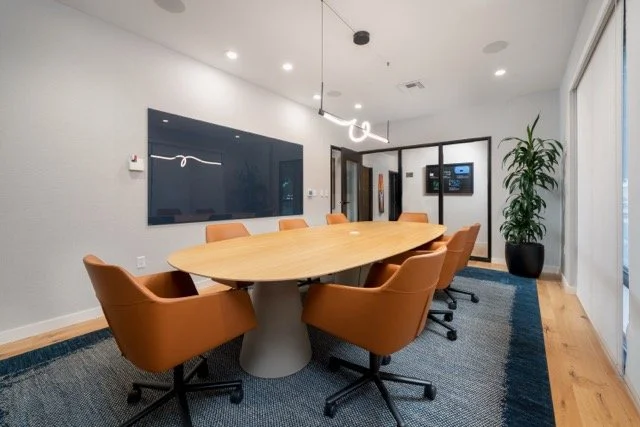 Modern conference room in Hillsboro, Oregon featuring a large white oak conference table, camel leather office chairs, a modern pendant light, and a wall-mounted writing board
