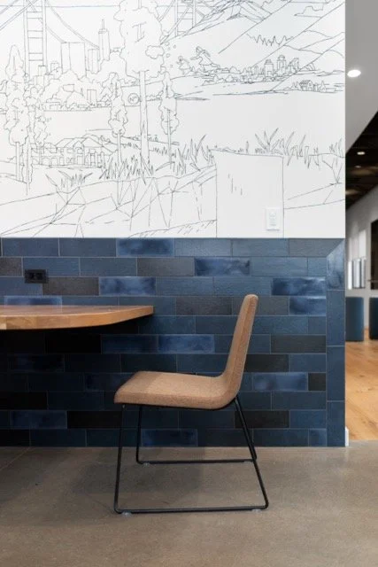 Creative office kitchen seating in Hillsboro, Oregon featuring a single seat and table in front of handmade tile wainscoting with a custom mural above for a tech firm