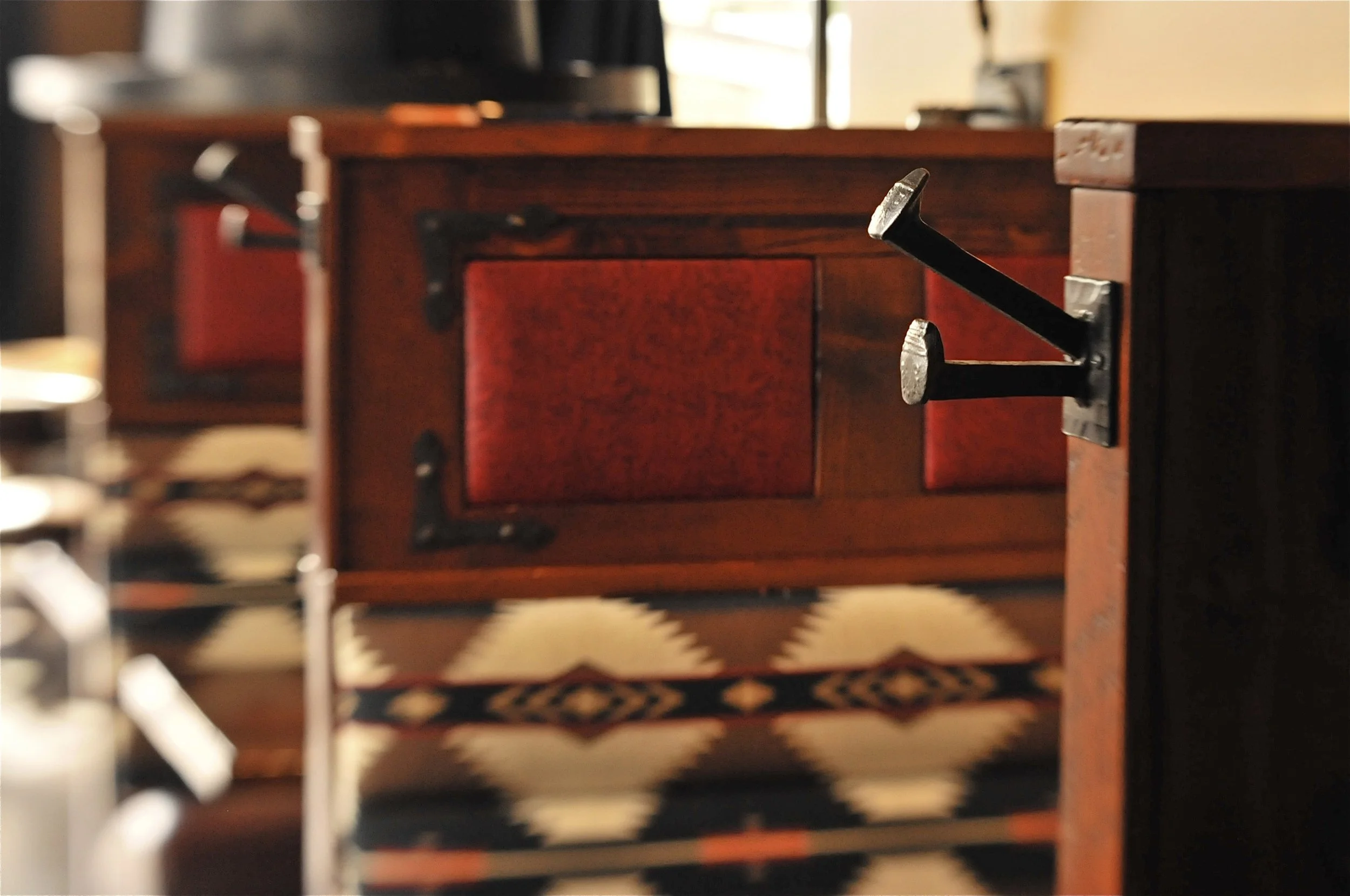 Southwest-inspired restaurant booth detail in Lake Oswego, Oregon featuring native-patterned upholstery, warm wood, custom wrought iron accents, and railroad spikes repurposed as coat hooks