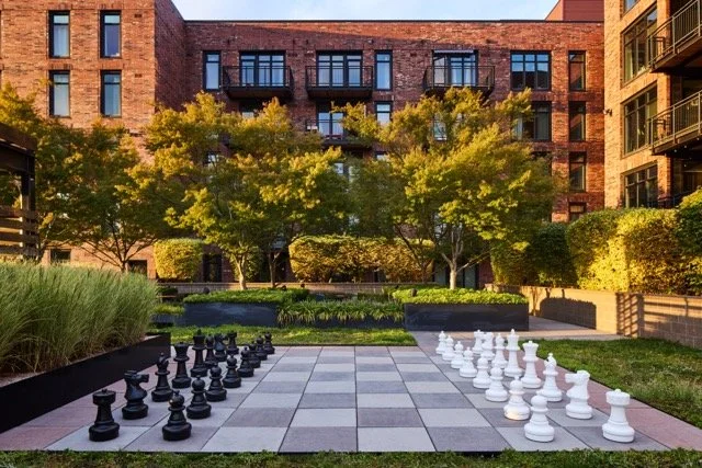 Large outdoor rooftop chessboard with black and white chess pieces, surrounded by greenery and trees, atop a multifamily commercial building in Portland, Oregon, designed by Weedman Design Partners