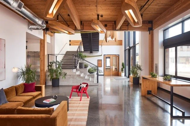 Modern commercial building lobby lounge in Vancouver, Washington featuring exposed wood beams and ceiling, a gold sectional sofa, and oversized potted plants