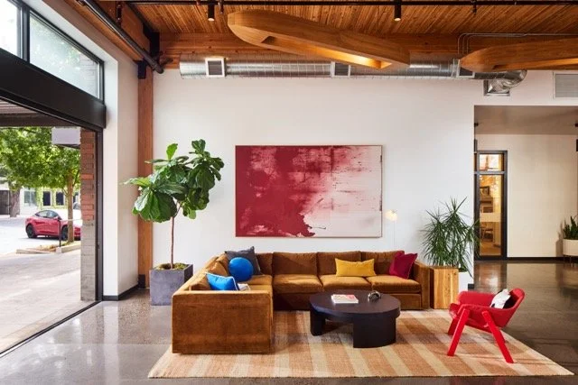 Commercial office lobby design in Vancouver, Washington featuring a roll-up glass garage door, gold sectional sofa, modern lounge seating, custom artwork, and large potted plants