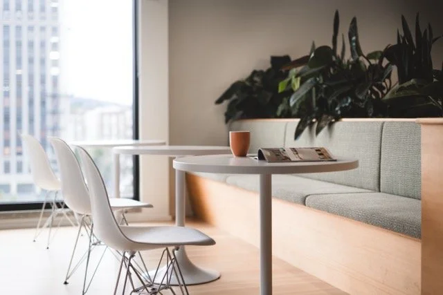 Modern commercial office breakout seating area featuring a light wood banquette with pale green upholstery, biophilic design elements, and sweeping city views of Portland through floor-to-ceiling windows