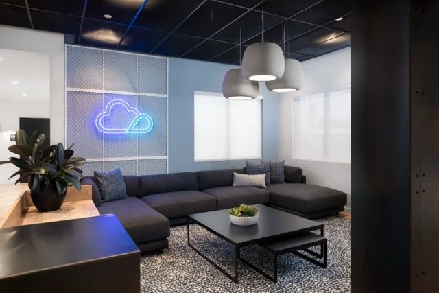 Creative office lobby in Hillsboro, Oregon featuring custom neon logo signage, a large dark gray sectional sofa, and modern pendant lighting