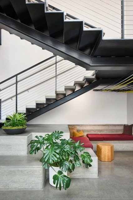 Modern entry in a commercial office building in Vancouver, Washington featuring an open steel staircase, tiered concrete seating, and biophilic design elements