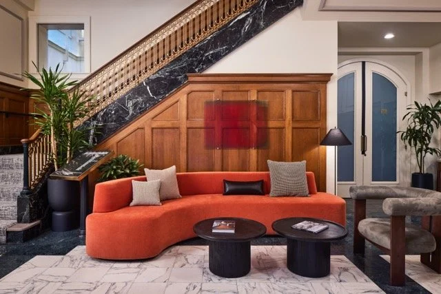 Modern lobby design for a historic commercial office building in downtown Portland, Oregon, featuring a custom burnt orange sectional, marble and wood stair banister, and large potted plants