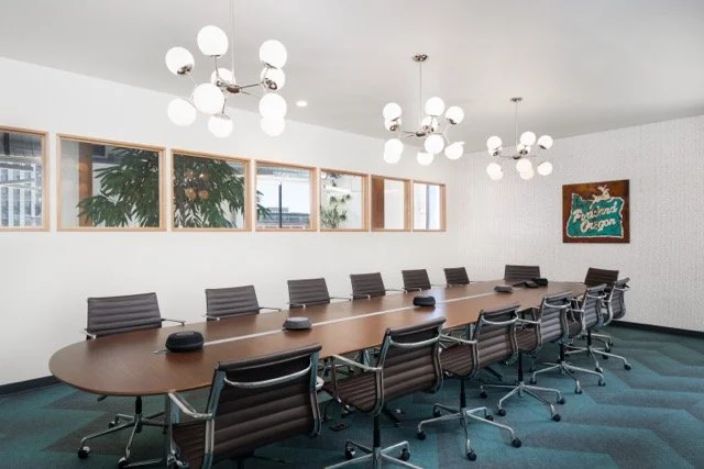 Conference room in modern commercial office in Portland, Oregon featuring atomic-style pendant lighting, interior windows overlooking biophilic design elements, Eames Aluminum Group office chairs, and a large walnut conference table