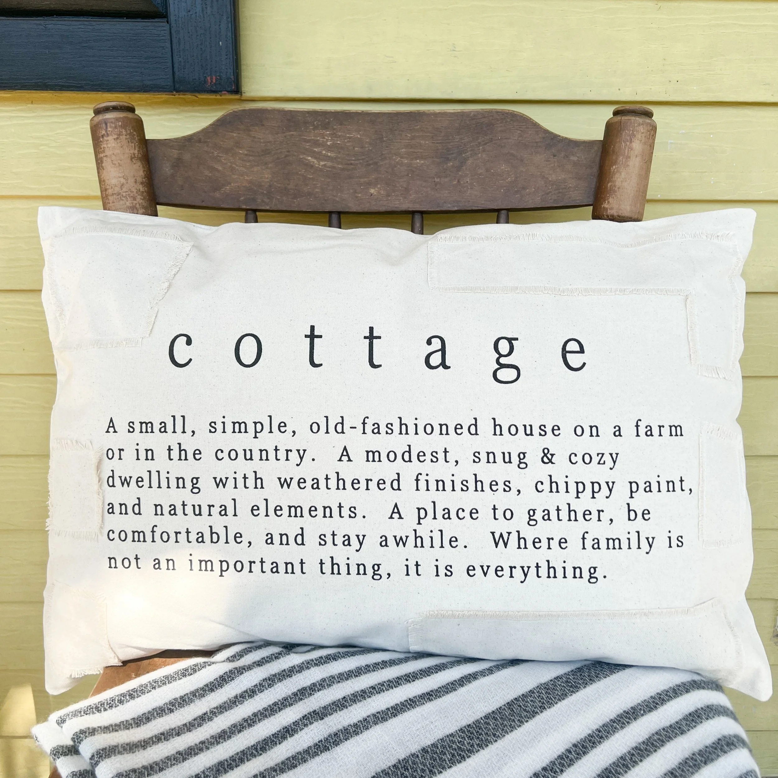 Decorative pillow with the word 'cottage' and a definition, placed on a chair with a striped fabric.