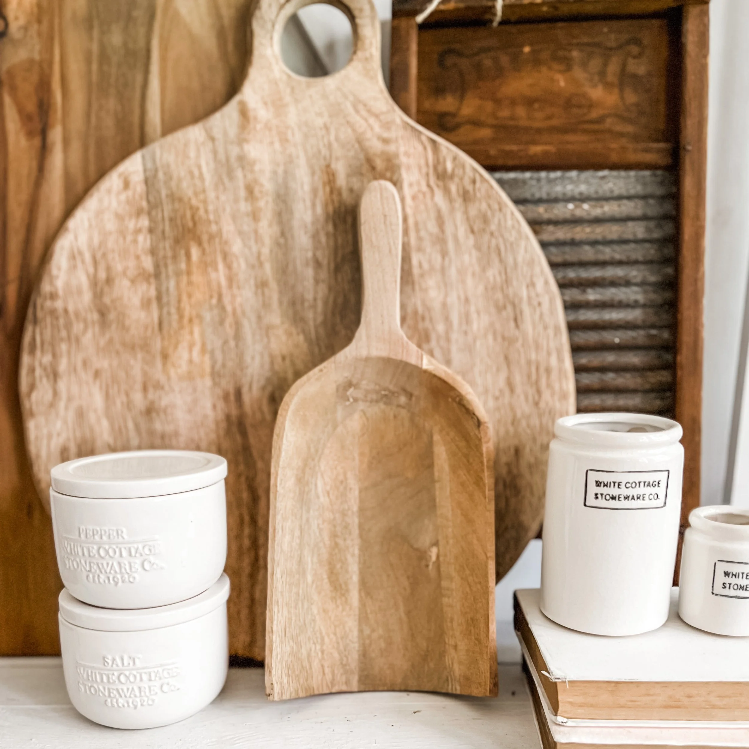Wooden cutting boards and scoops, and white ceramic jars labeled 'pepper,' 'salt,' and other kitchen items, arranged on a white surface with a wooden background.