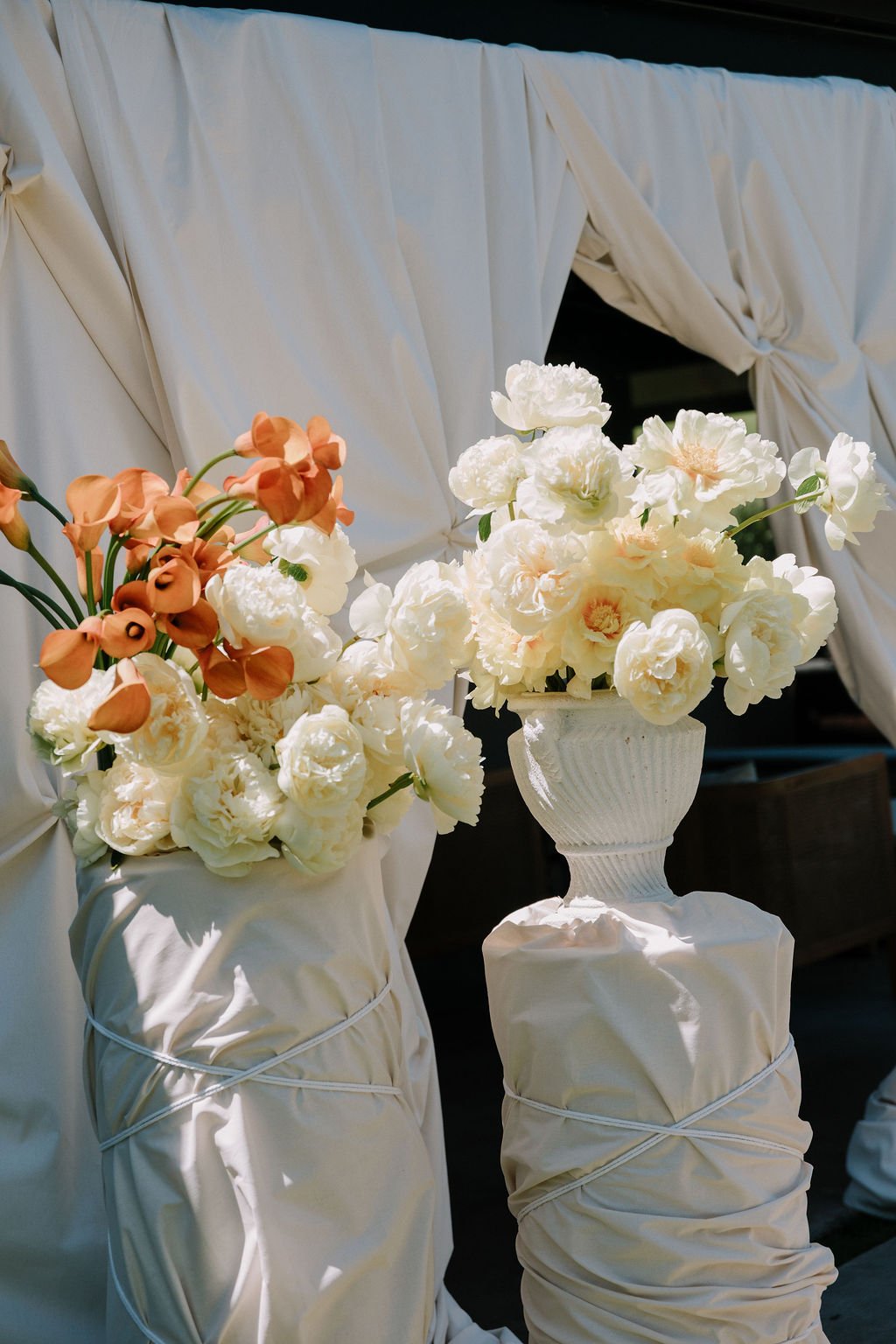 Sculptural white and orange wedding flowers styled by LVR Bridal with draped fabric wrapped plinths and vintage vases