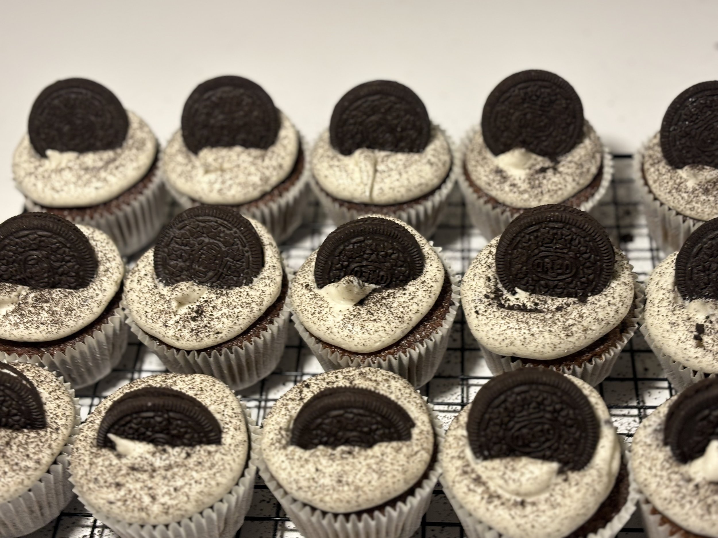 A batch of Oreo cupcake treats topped with Oreo cookie halves on whipped frosting, arranged on a cooling rack.