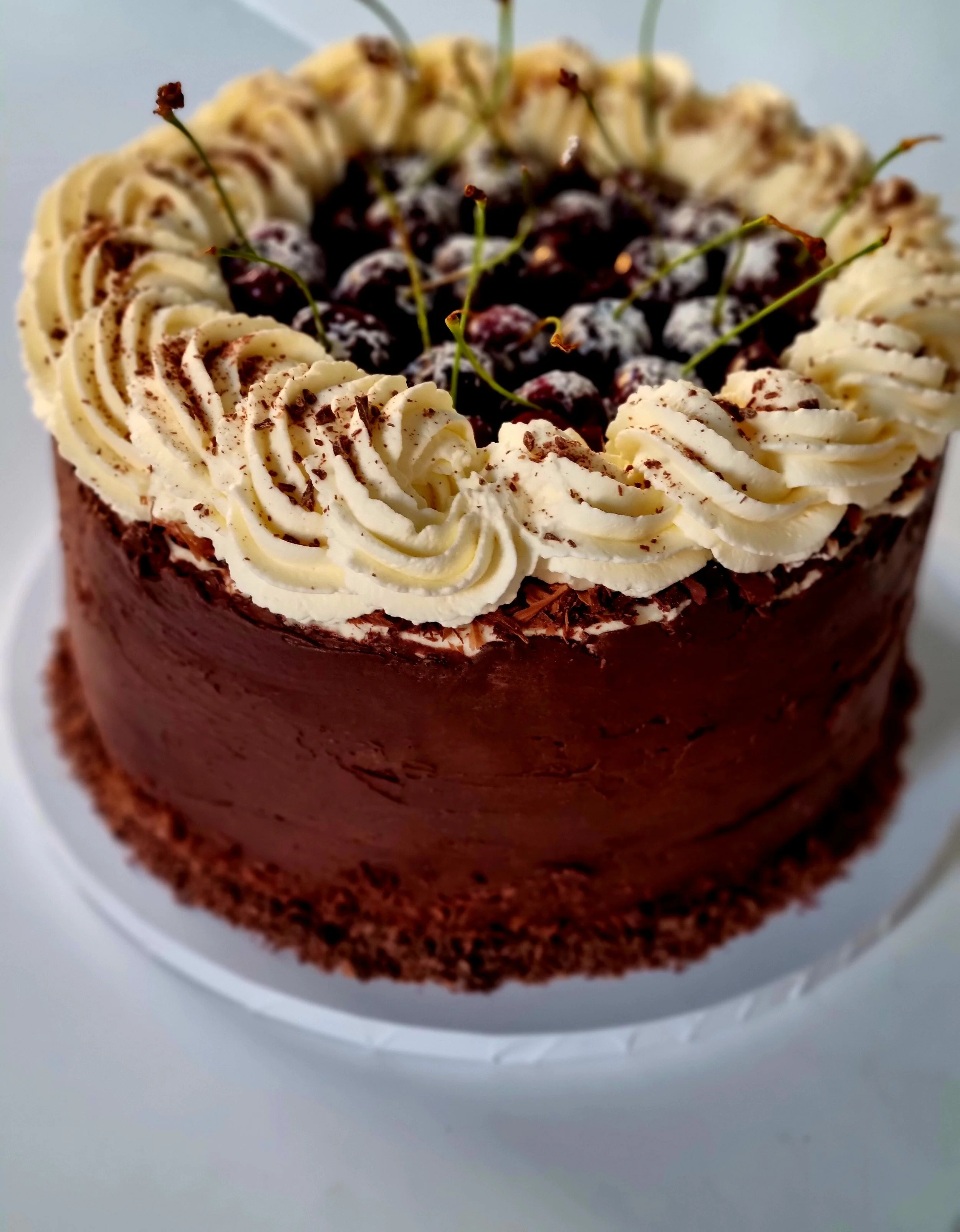 Chocolate birthday cake with whipped cream swirls and cherries on top.
