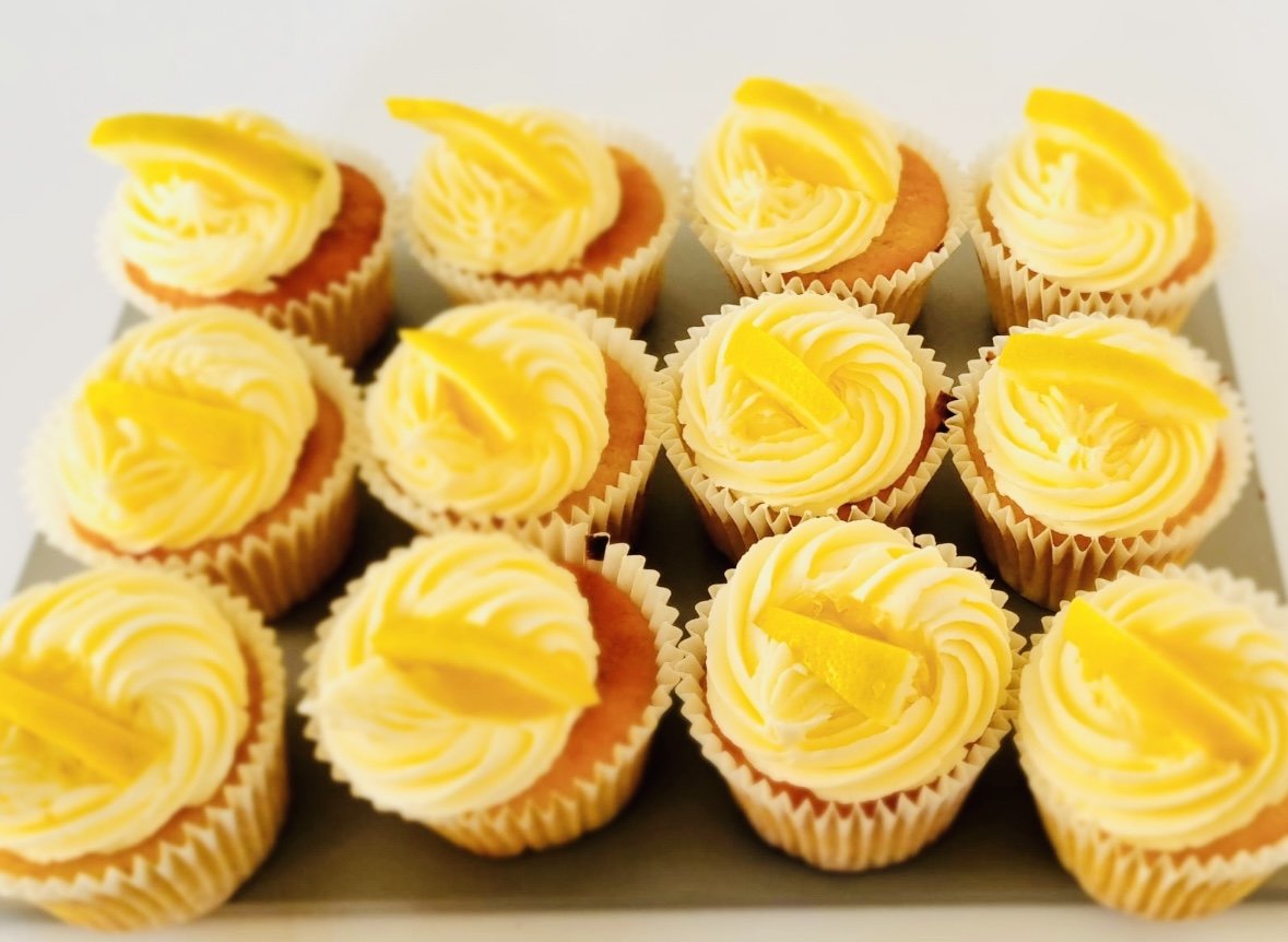 Lemon cupcakes with yellow frosting and lemon peel garnish, arranged on a white tray.