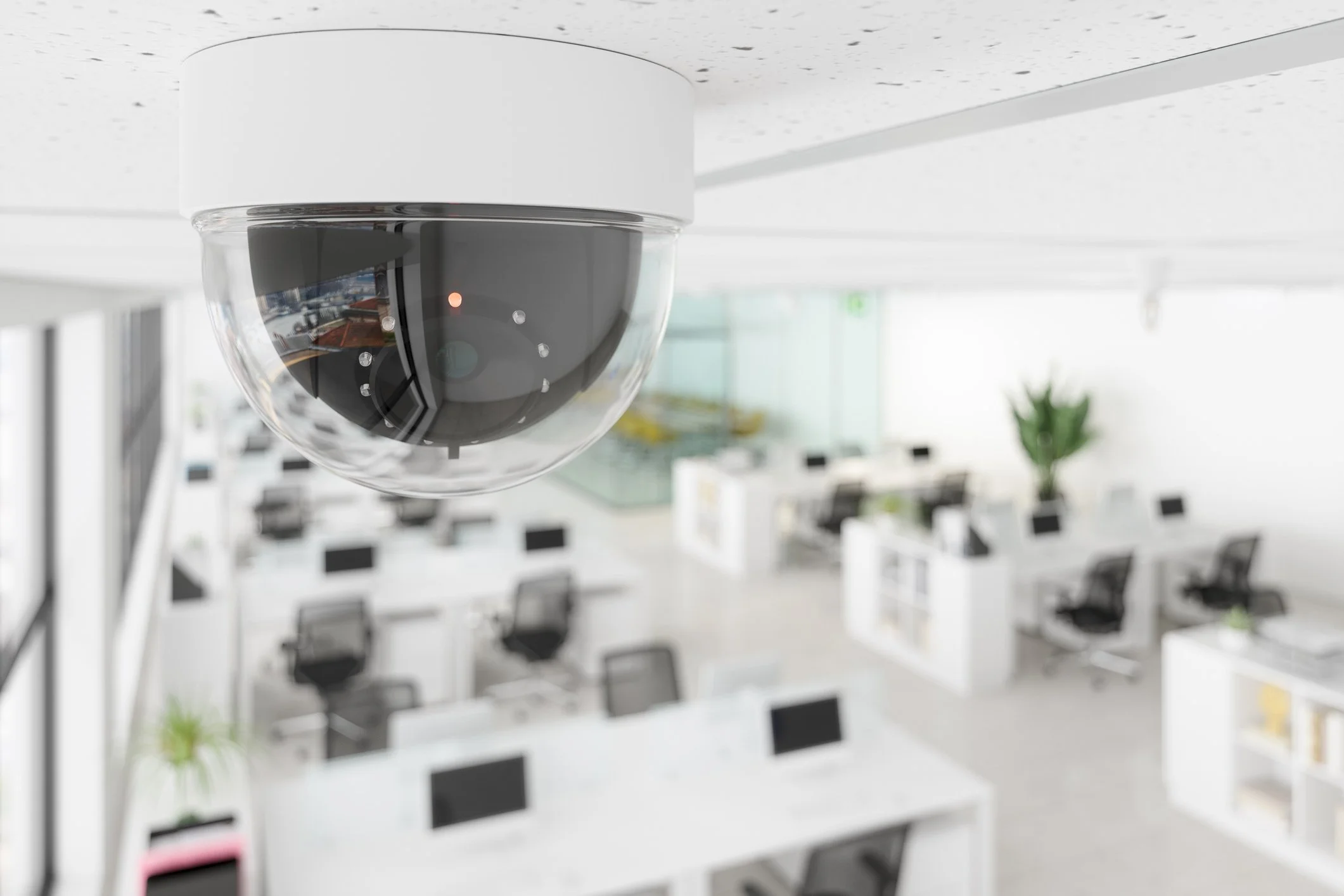 Dome security camera mounted on an office ceiling overlooking an open-plan workspace