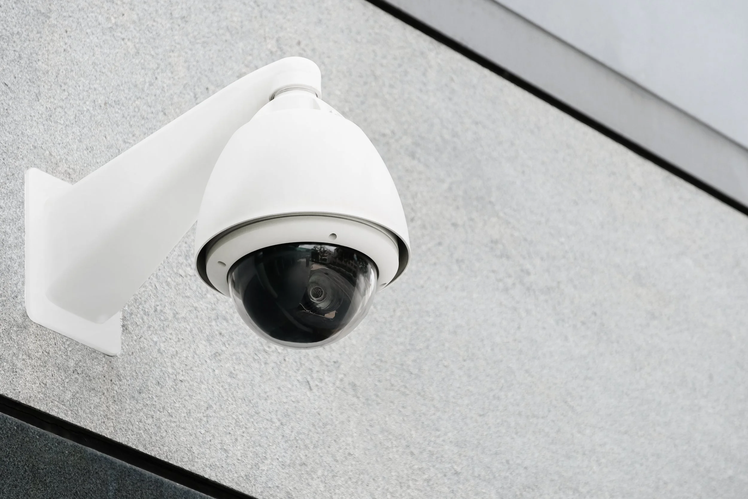 White dome security camera mounted on a concrete exterior wall