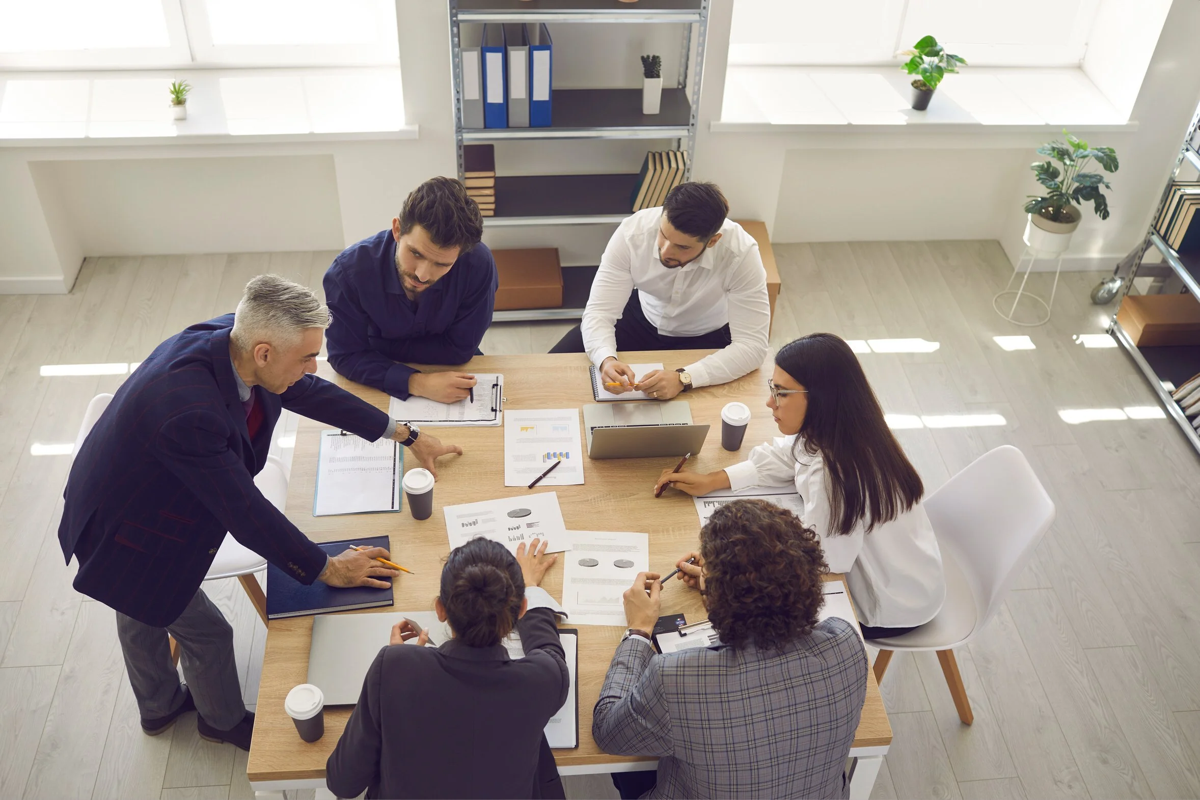 Overhead view of five business professionals collaborating around a conference table with documents and a laptop