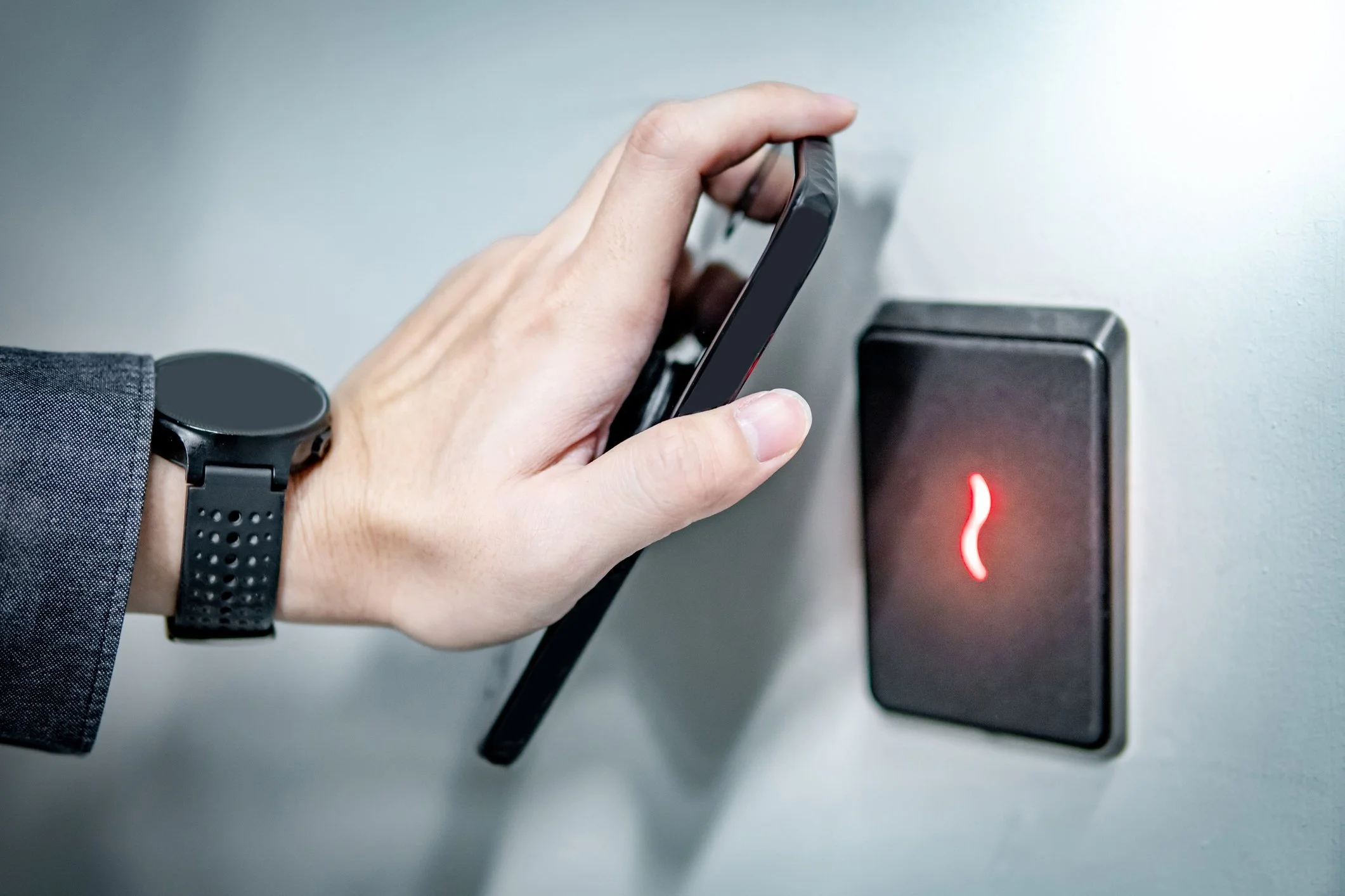 Person holding a smartphone near a black NFC access control reader with a red indicator light