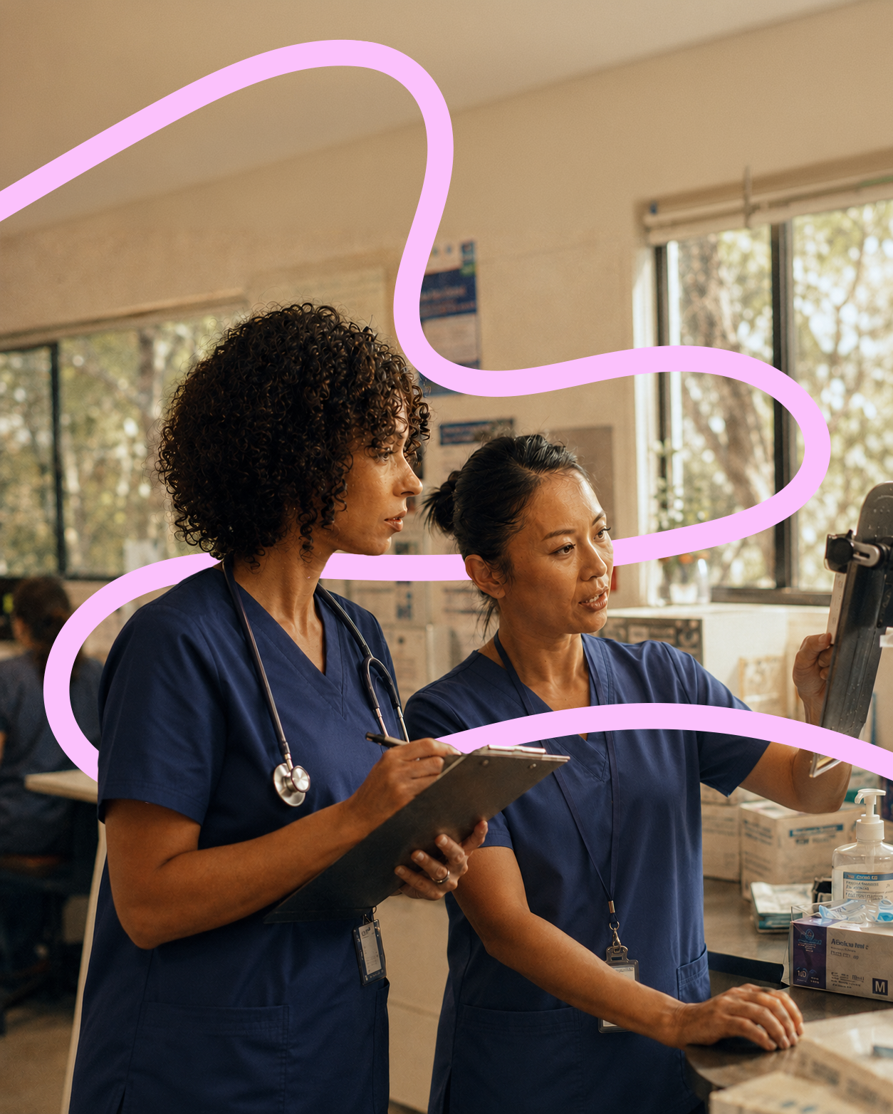 Two female healthcare workers in navy scrubs working together in a hospital or clinic, one holding a clipboard and the other adjusting a device.
