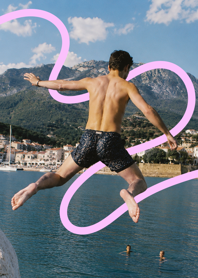A young man is jumping into a body of water near a coastal town with mountains in the background. He is shirtless and wearing dark swim trunks, with two people swimming in the water below. There is a pink, neon-like digital line swirl around him.