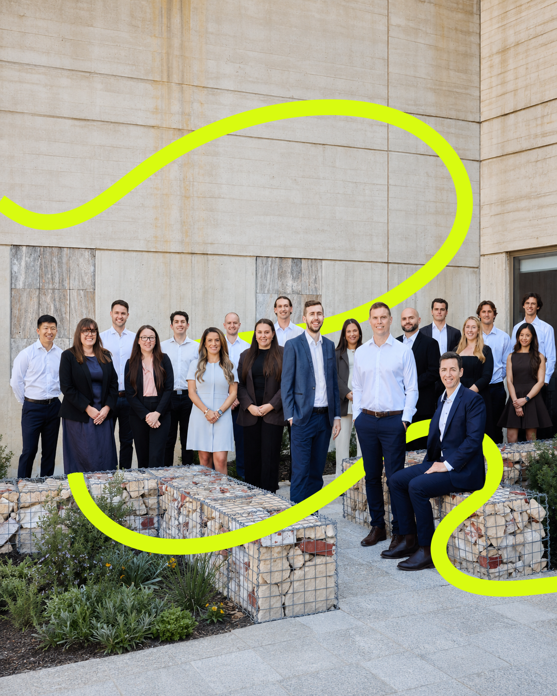 Group of business professionals standing outdoors in front of a modern building with concrete walls, some smiling, dressed in formal business attire.